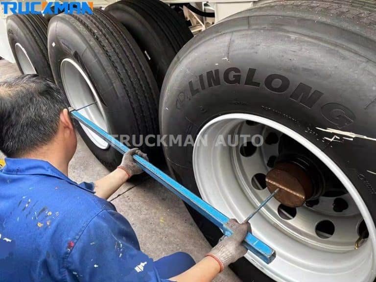 Maintenance technician is checking and maintaining tyre pressure on a low-bed semi-trailer, using tools to ensure tyre screws are tight