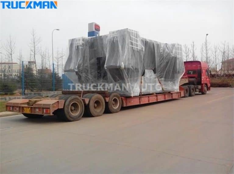 Low-bed semi-trailer transporting large covered industrial equipment.