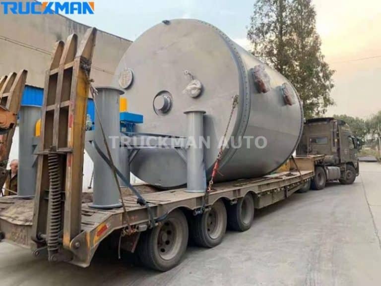 Heavy-duty low-bed semi-trailer hauling an oversized industrial storage tank.