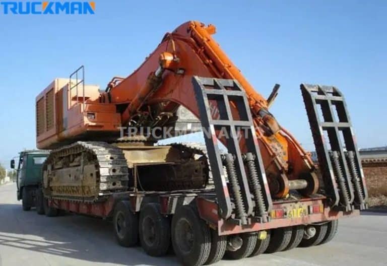 Low-bed semi-trailer with deployed ramps loading an orange tracked excavator.